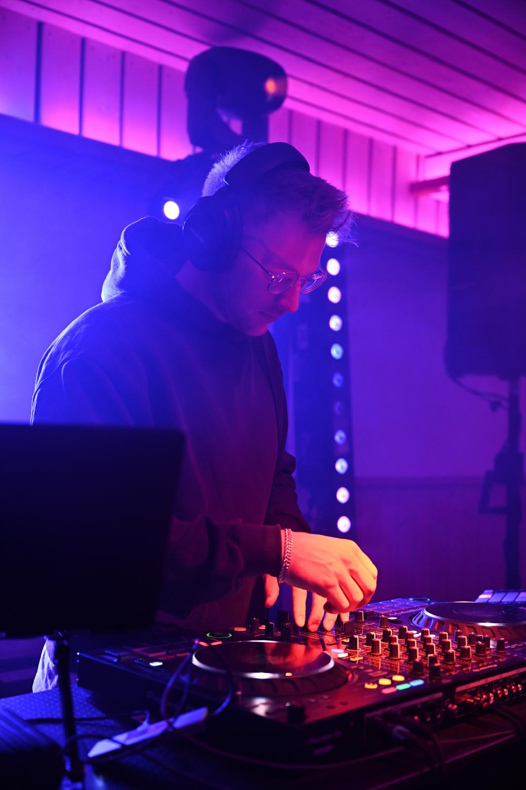 DJ mit Kopfhörer am Pioneer-Pult in violettem Licht