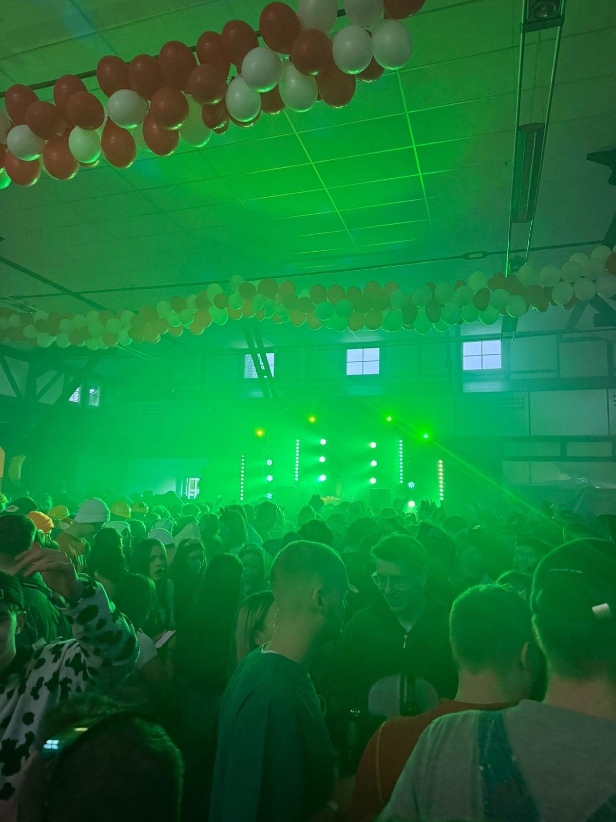 Volle Halle mit tanzenden Gästen in grünem Licht, Ballongirlanden unter der Decke