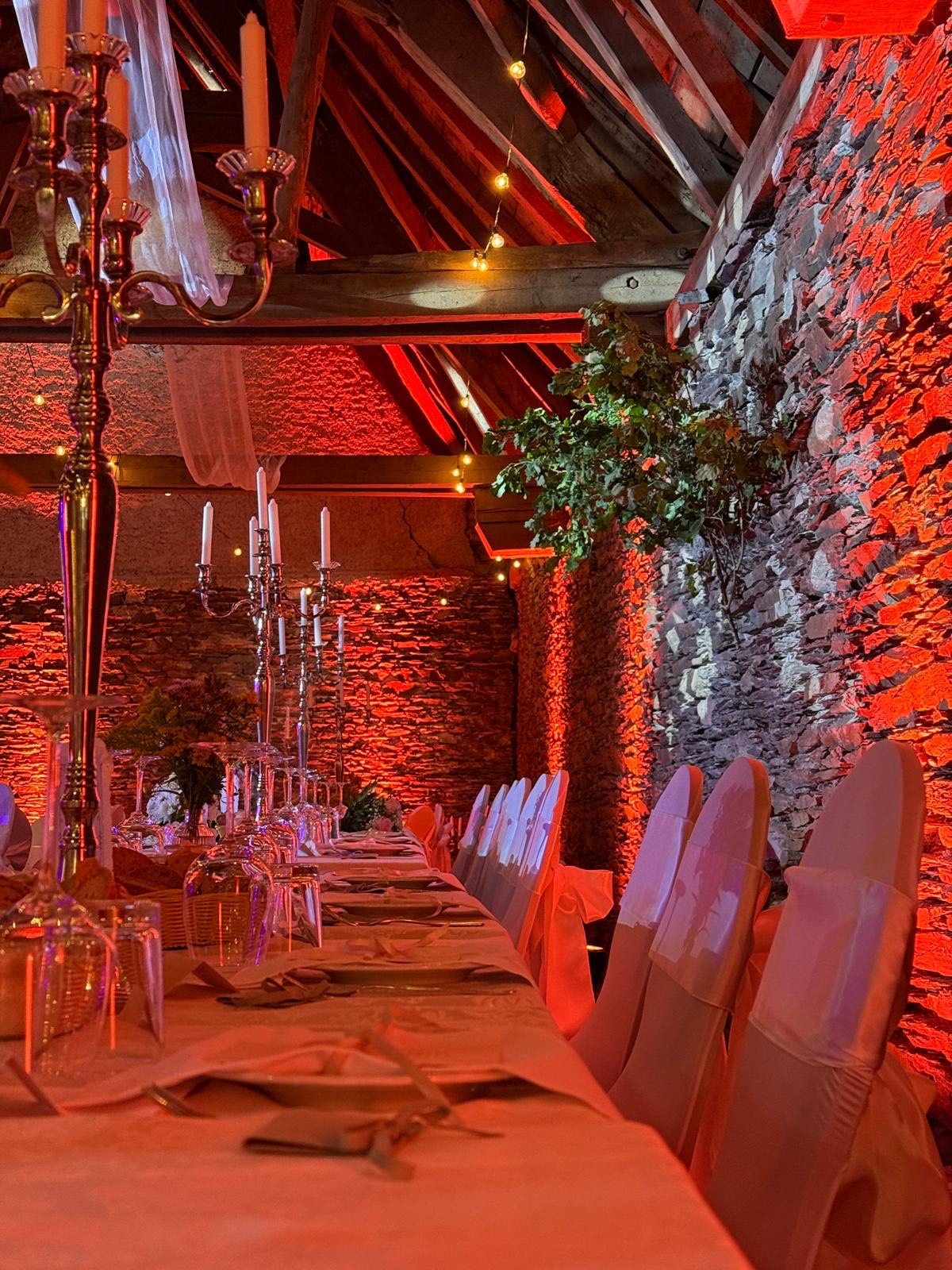 Lange Festtafel in einer Scheune, Natursteinwände in rotem Licht angestrahlt